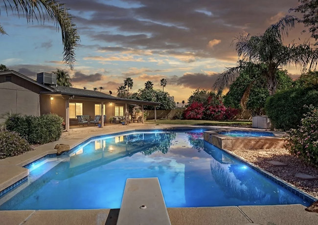 A Scottsdale home with an illuminated backyard pool at sunset